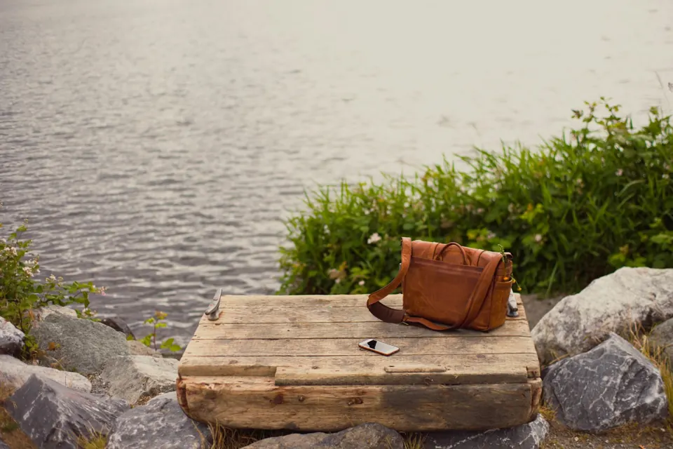 Brown leather crossbody bag on brown wooden panel near water