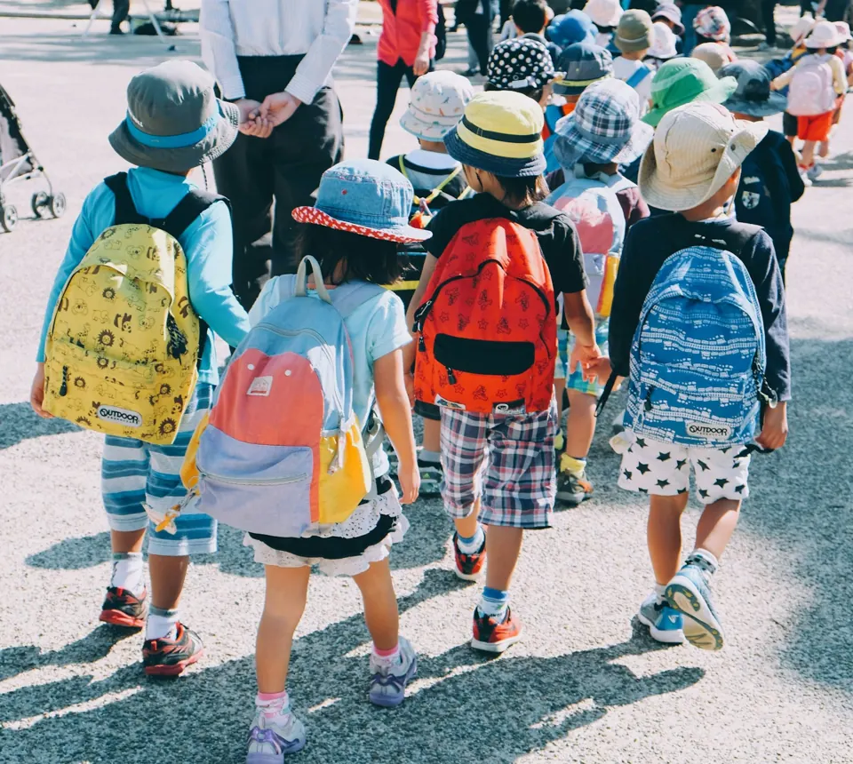 Group of people wearing white and orange backpacks walking on pavement