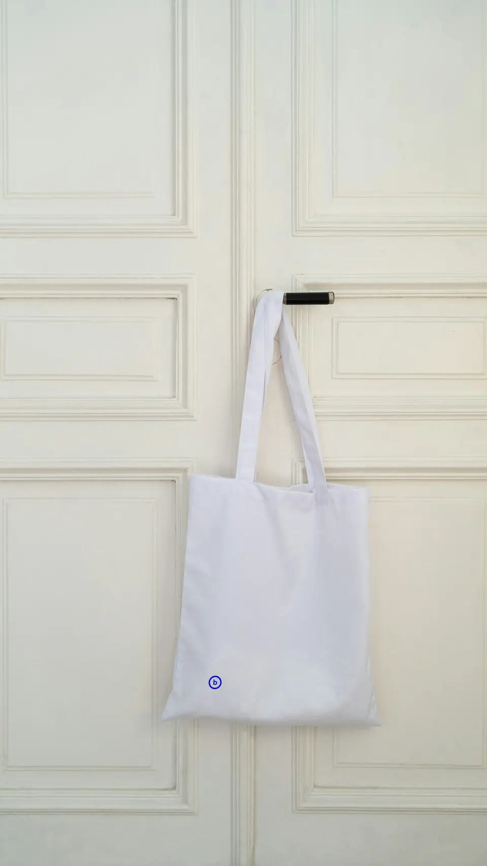 A white tote bag hanging on a white door